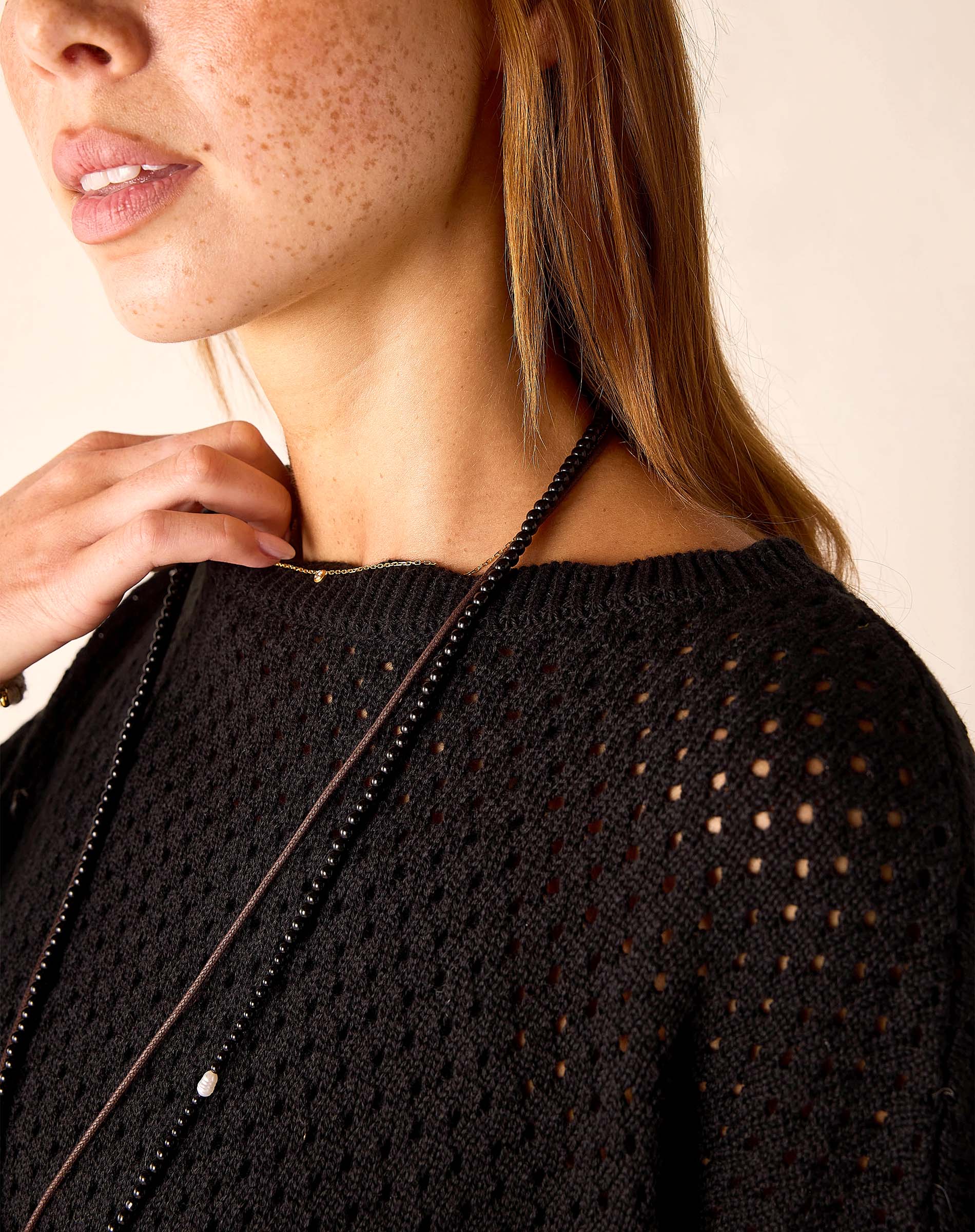 Close-up of a person wearing a black knit sweater with a beige background