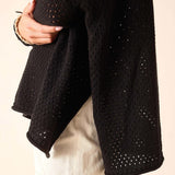 Black knitted cardigan with a textured pattern worn by a person on a beige background