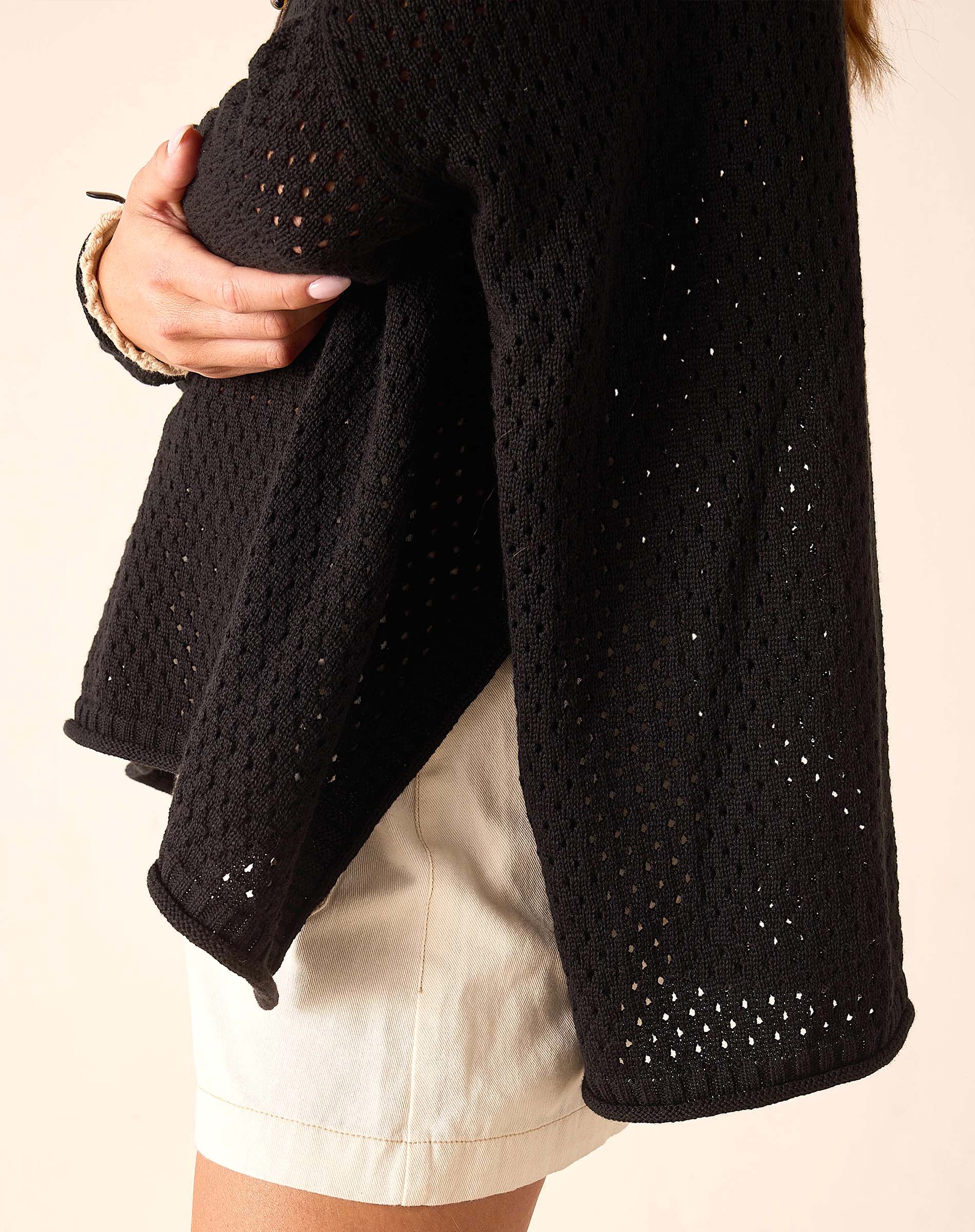 Black knitted cardigan with a textured pattern worn by a person on a beige background