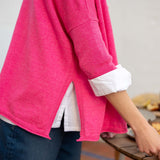 Fuchsia knit top with ruffled details and a layered white shirt underneath.
