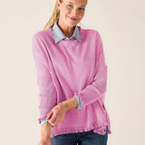 Woman wearing a pink sweater with rolled-up sleeves and blue jeans on a plain background
