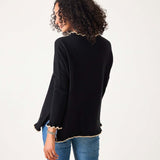 Back view of the black and taupe ruffled knit sweater with a scalloped hem over blue denim jeans.