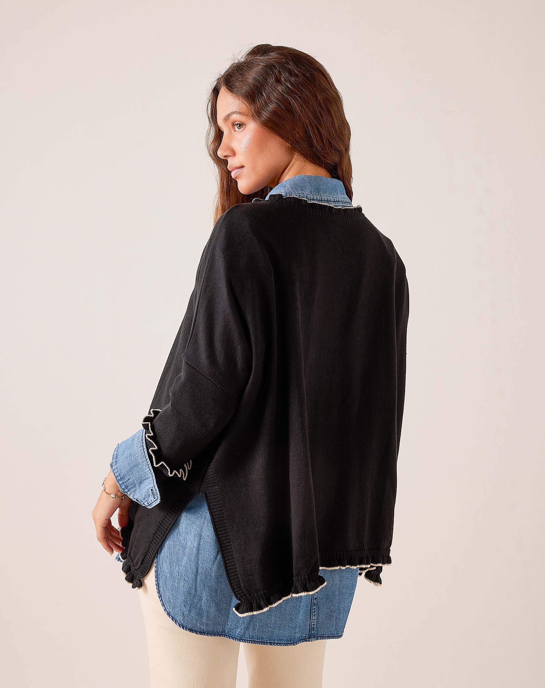 Black oversized knit sweater with ruffled sleeve details and frayed hemline shown from the back view