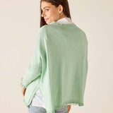 Woman wearing a light green cardigan over a white shirt on a beige background