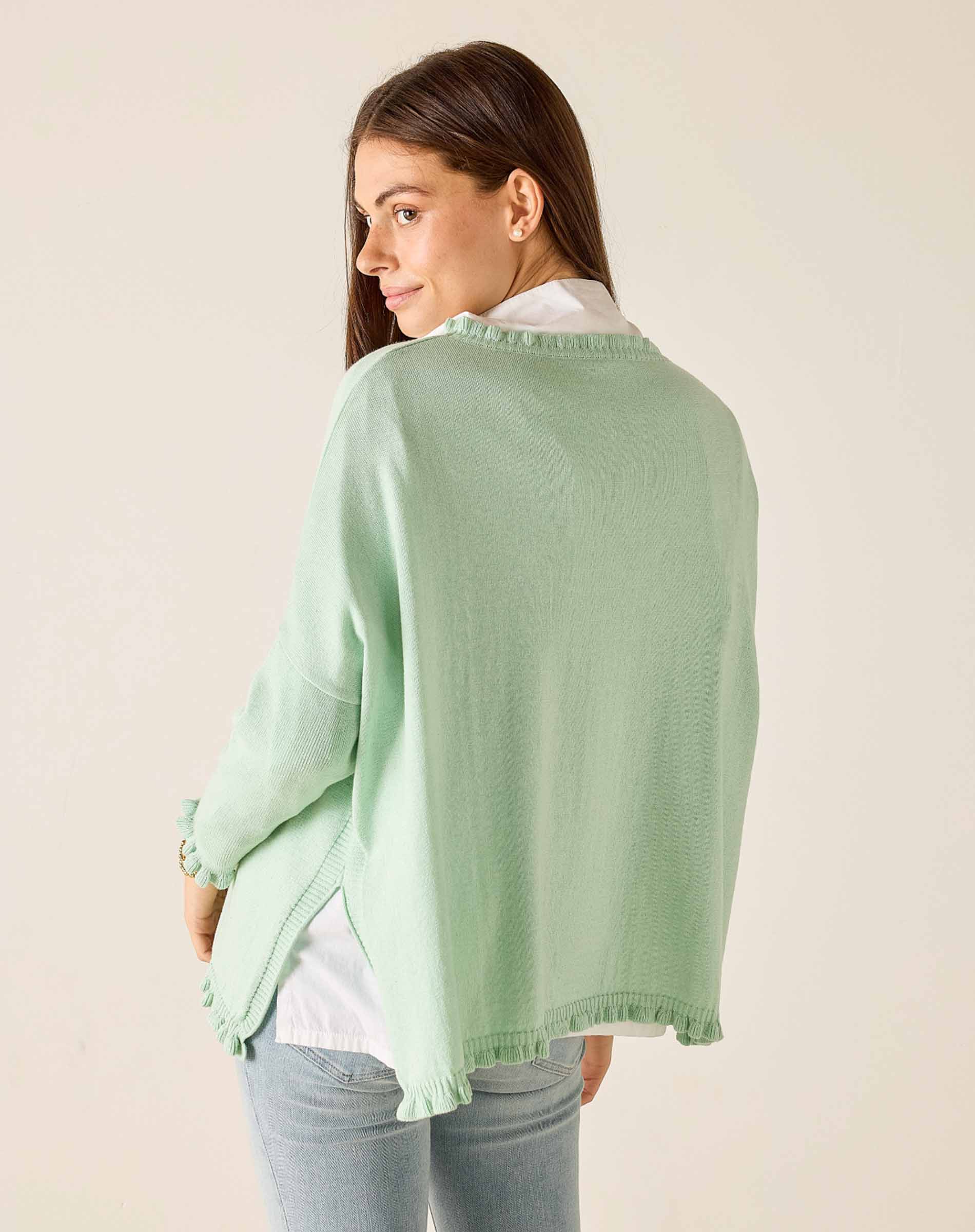 Woman wearing a light green cardigan over a white shirt on a beige background