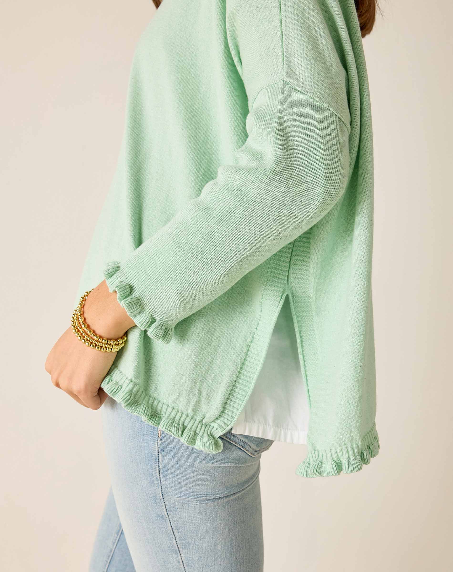 Person wearing a light green sweater with ruffled cuffs on a plain background