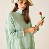 Woman wearing a light green sweater holding a red tulip against a plain background