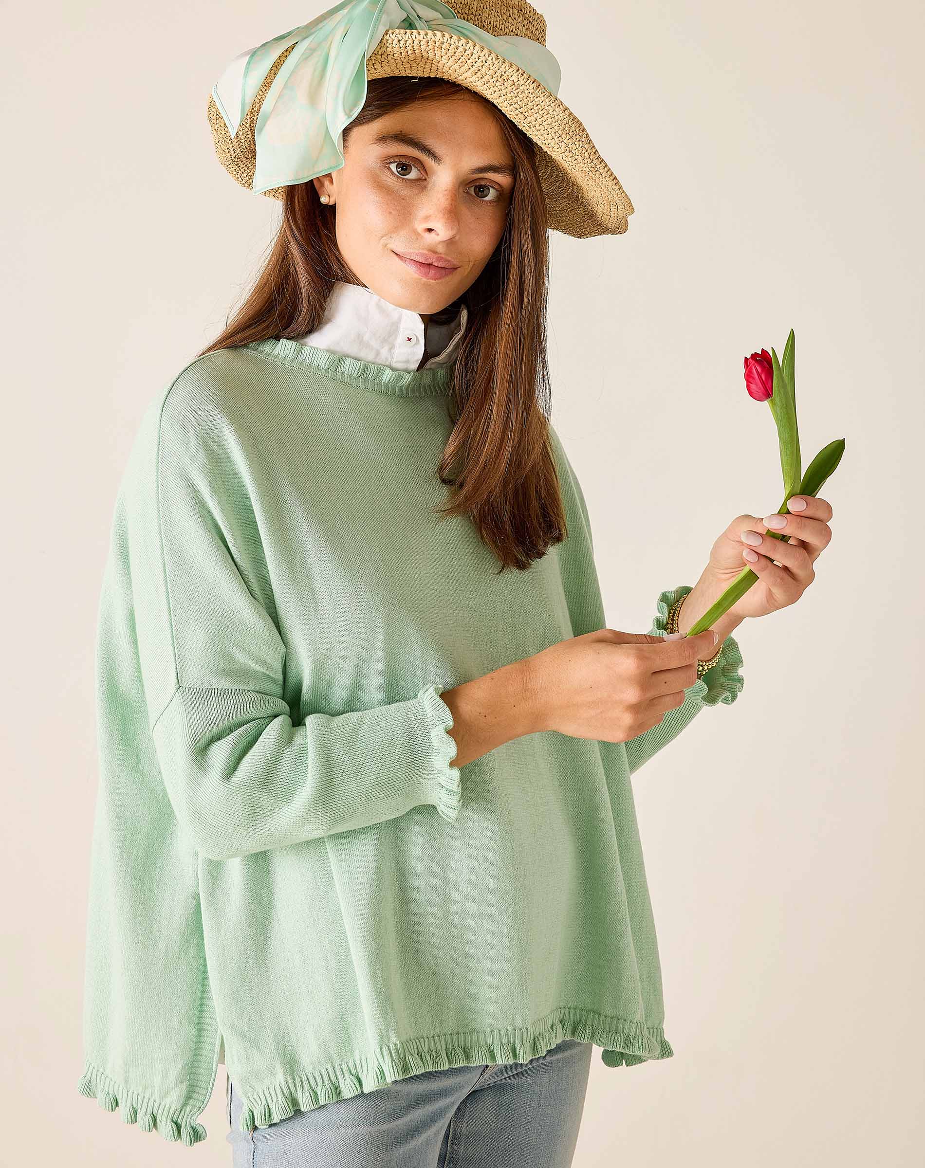 Woman wearing a light green sweater holding a red tulip against a plain background