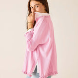 Woman wearing a pink sweater with a white shirt underneath on a beige background
