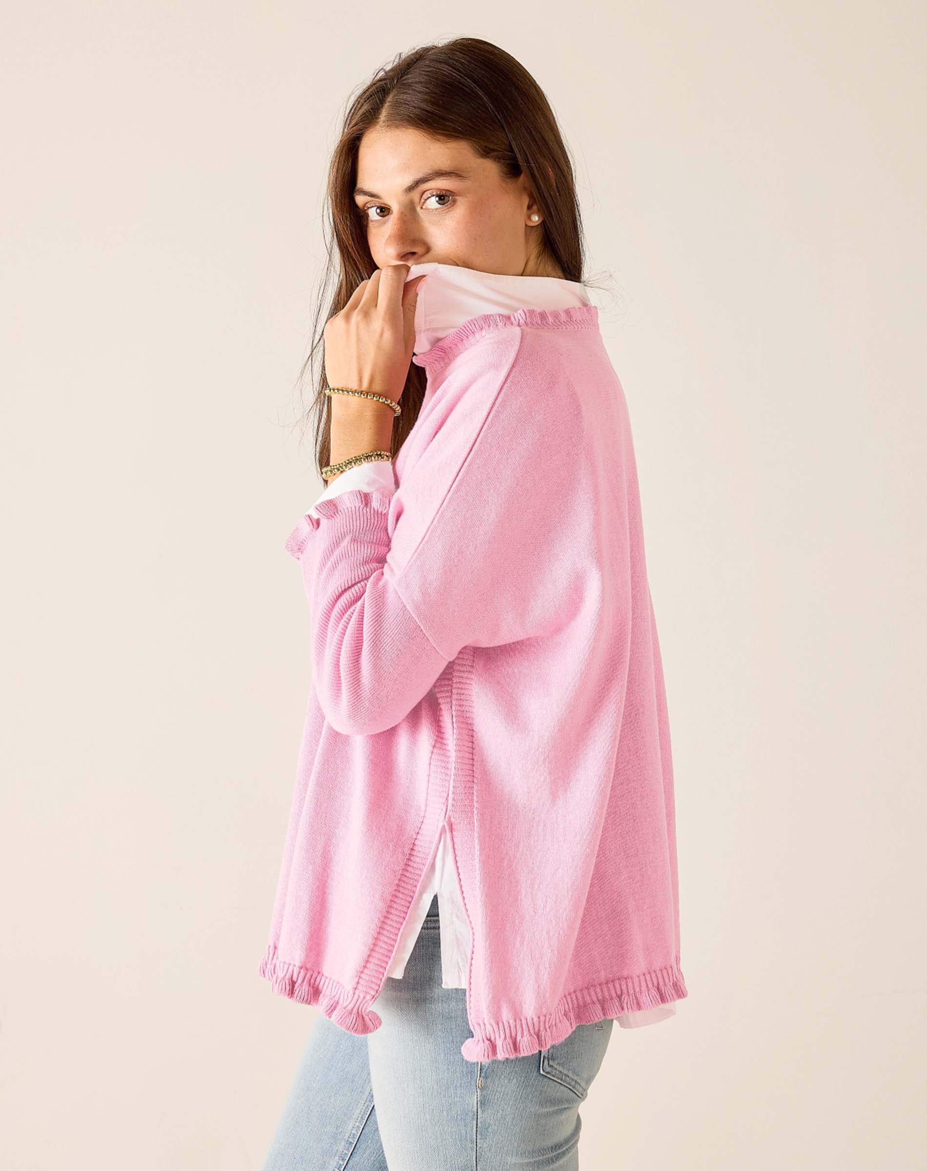 Woman wearing a pink sweater with a white shirt underneath on a beige background
