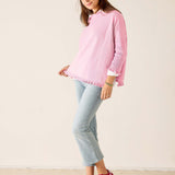 Woman wearing a pink sweater and light blue jeans against a white background