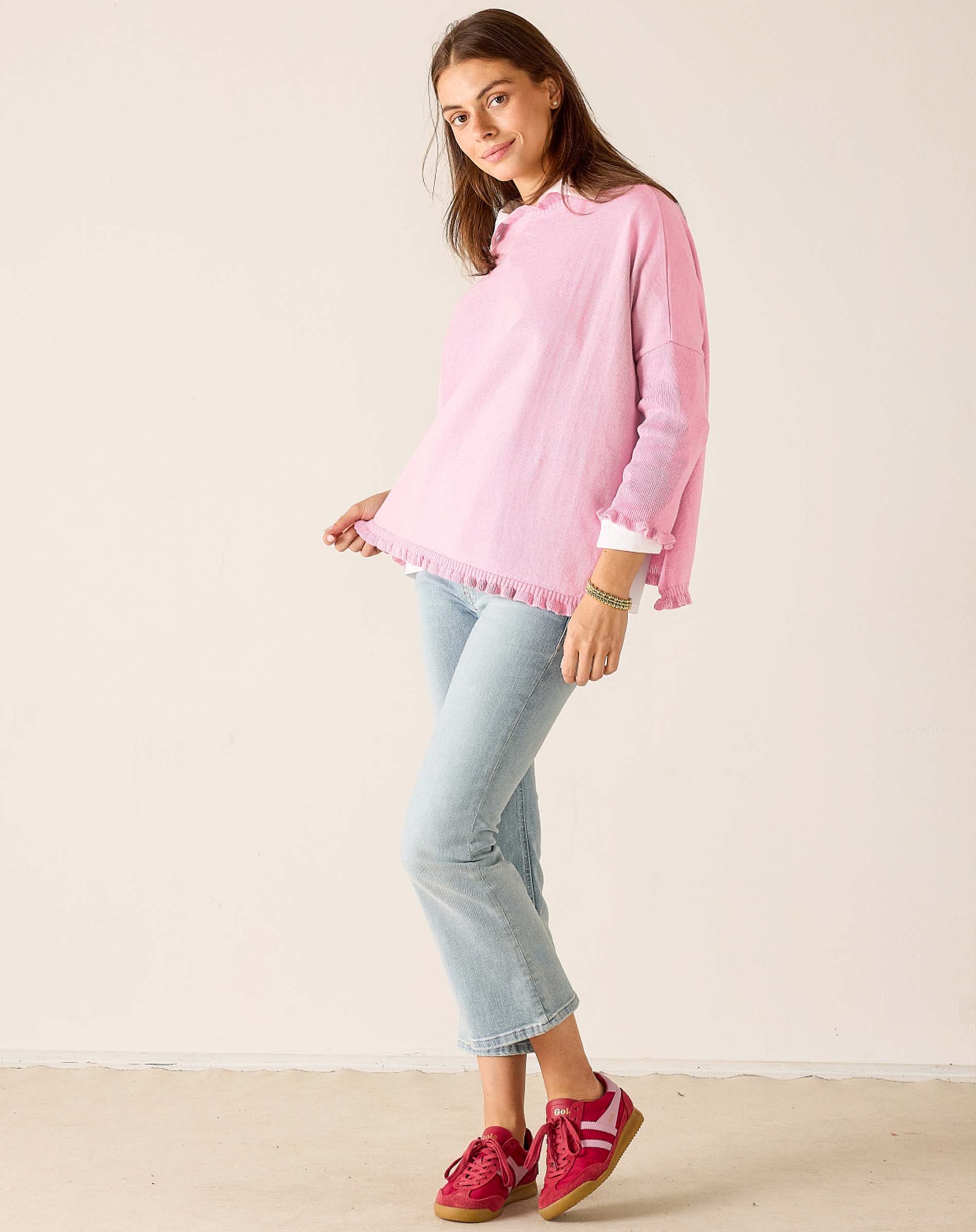 Woman wearing a pink sweater and light blue jeans against a white background