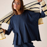 Woman wearing a navy blue outfit holding a striped sweater over her shoulder against a beige background