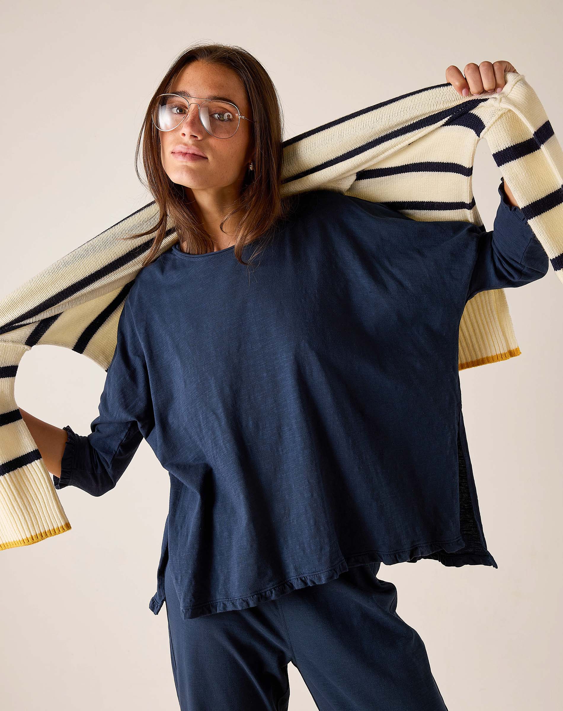 Woman wearing a navy blue outfit holding a striped sweater over her shoulder against a beige background