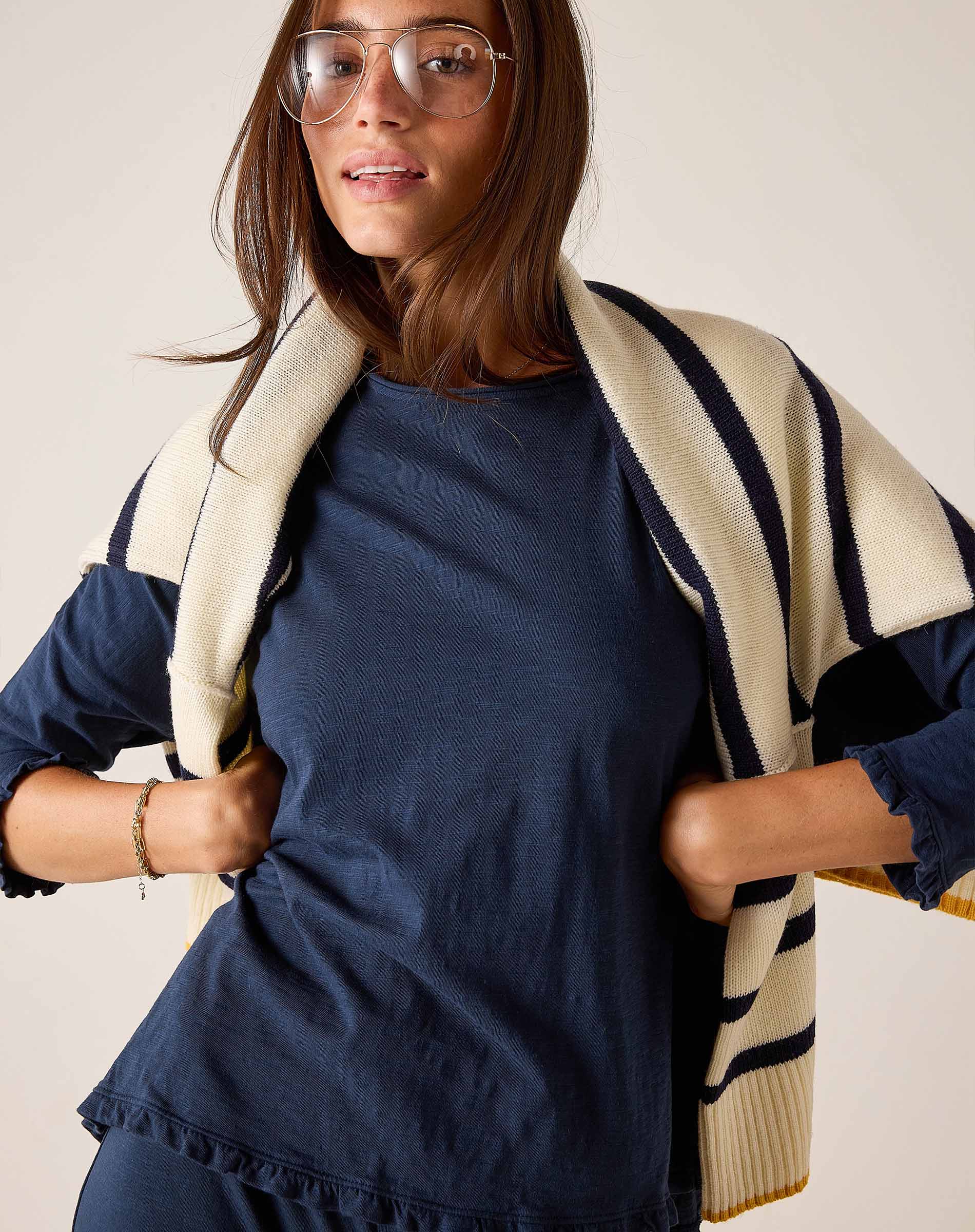 Woman wearing a navy dress with a beige and black striped cardigan against a plain background