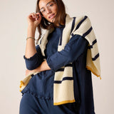 Woman wearing a navy outfit with a striped beige and navy shawl on a plain background