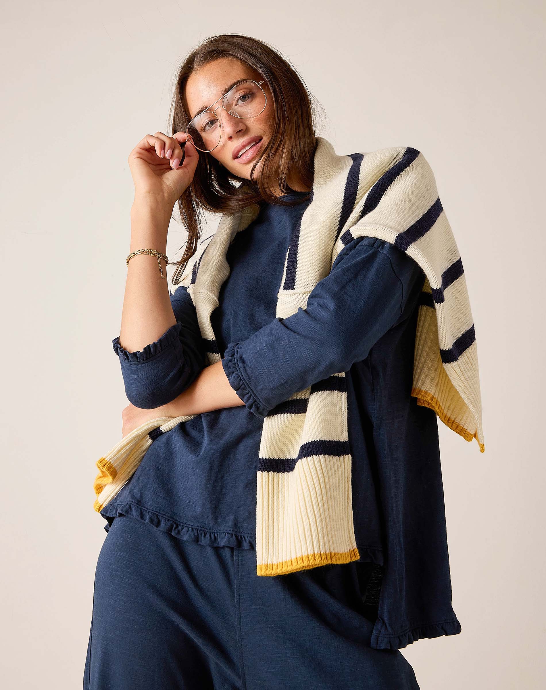 Woman wearing a navy outfit with a striped beige and navy shawl on a plain background