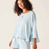 Woman wearing a light blue outfit with ruffled sleeves and shorts on a beige background