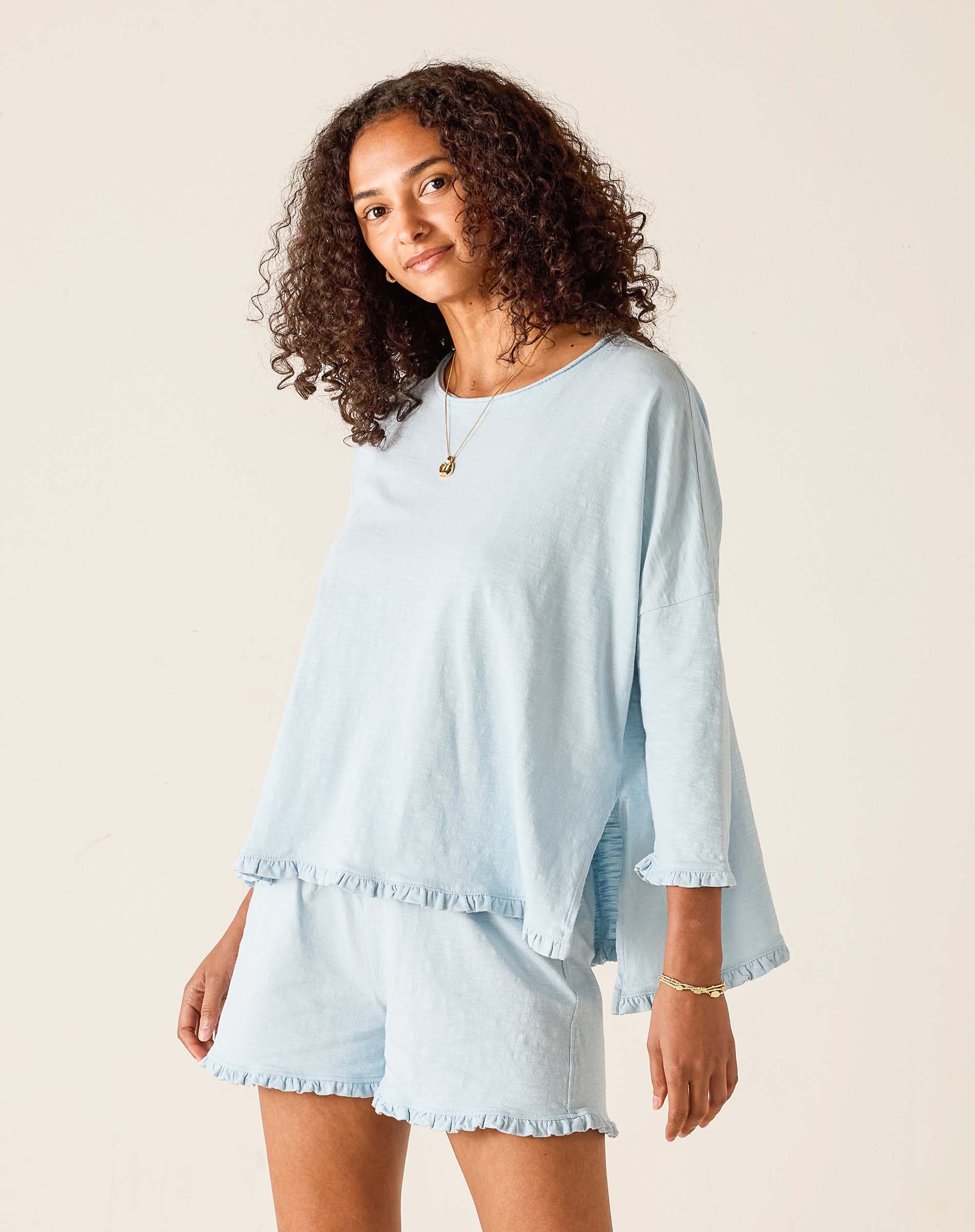 Woman wearing a light blue outfit with ruffled sleeves and shorts on a beige background