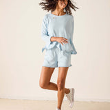 Woman wearing a light blue outfit with shorts and a top, standing against a plain background.