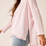 Person wearing a light pink blouse with long sleeves and a neutral background