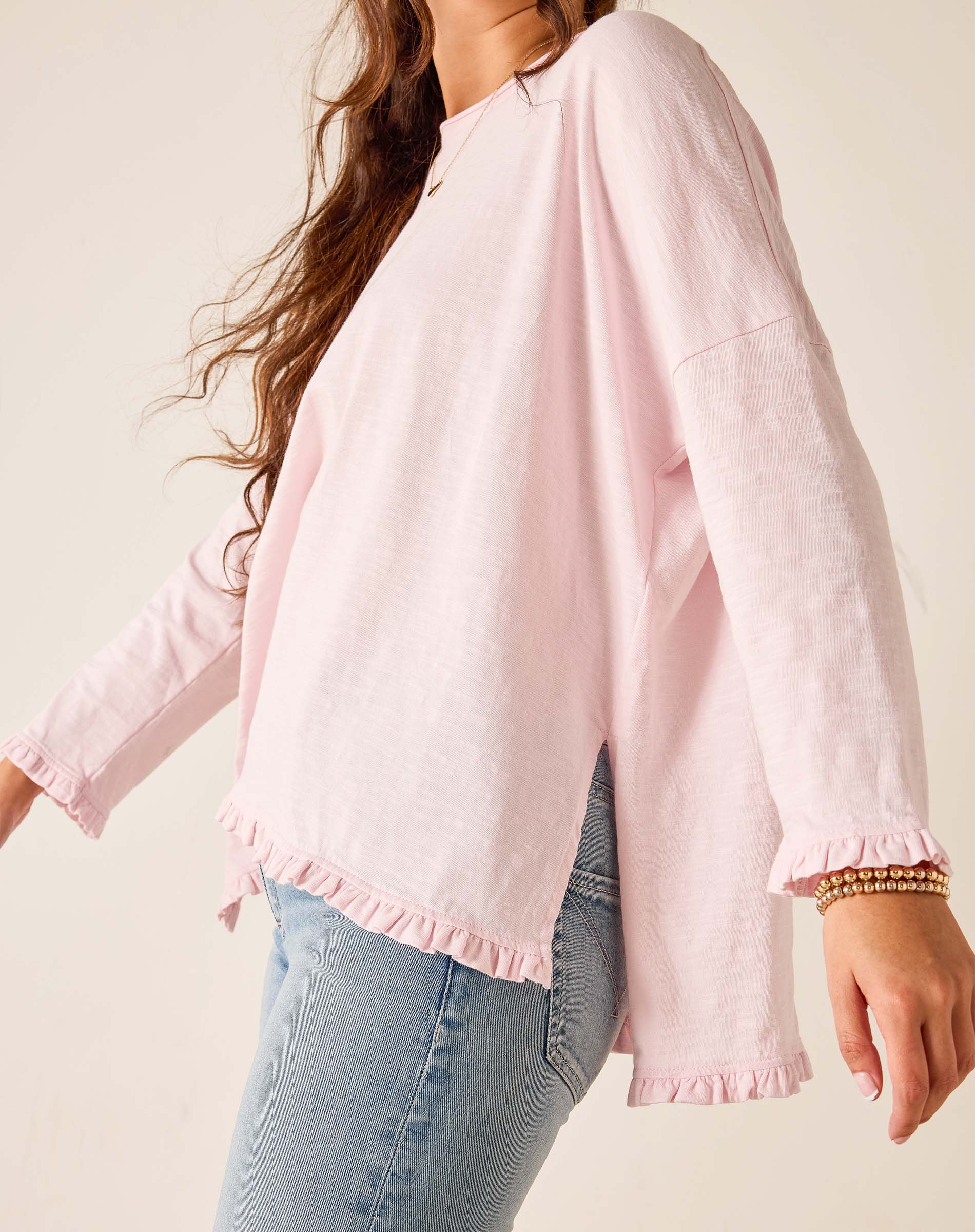 Person wearing a light pink blouse with long sleeves and a neutral background