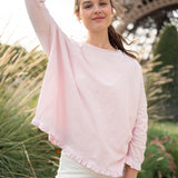 Woman wearing a light pink blouse with a blurred background of greenery and a structure.