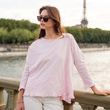 Woman in a pink top and white pants standing by a waterfront with the Eiffel Tower in the background.