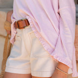 Person wearing a light pink long-sleeve top and beige shorts with a brown belt.