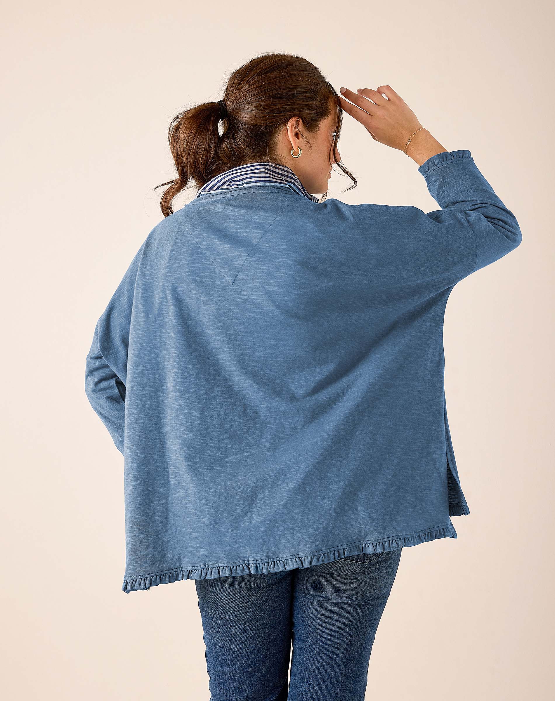 Back view of women's travel-friendly slate blue top with a ruffled hem and striped trim.