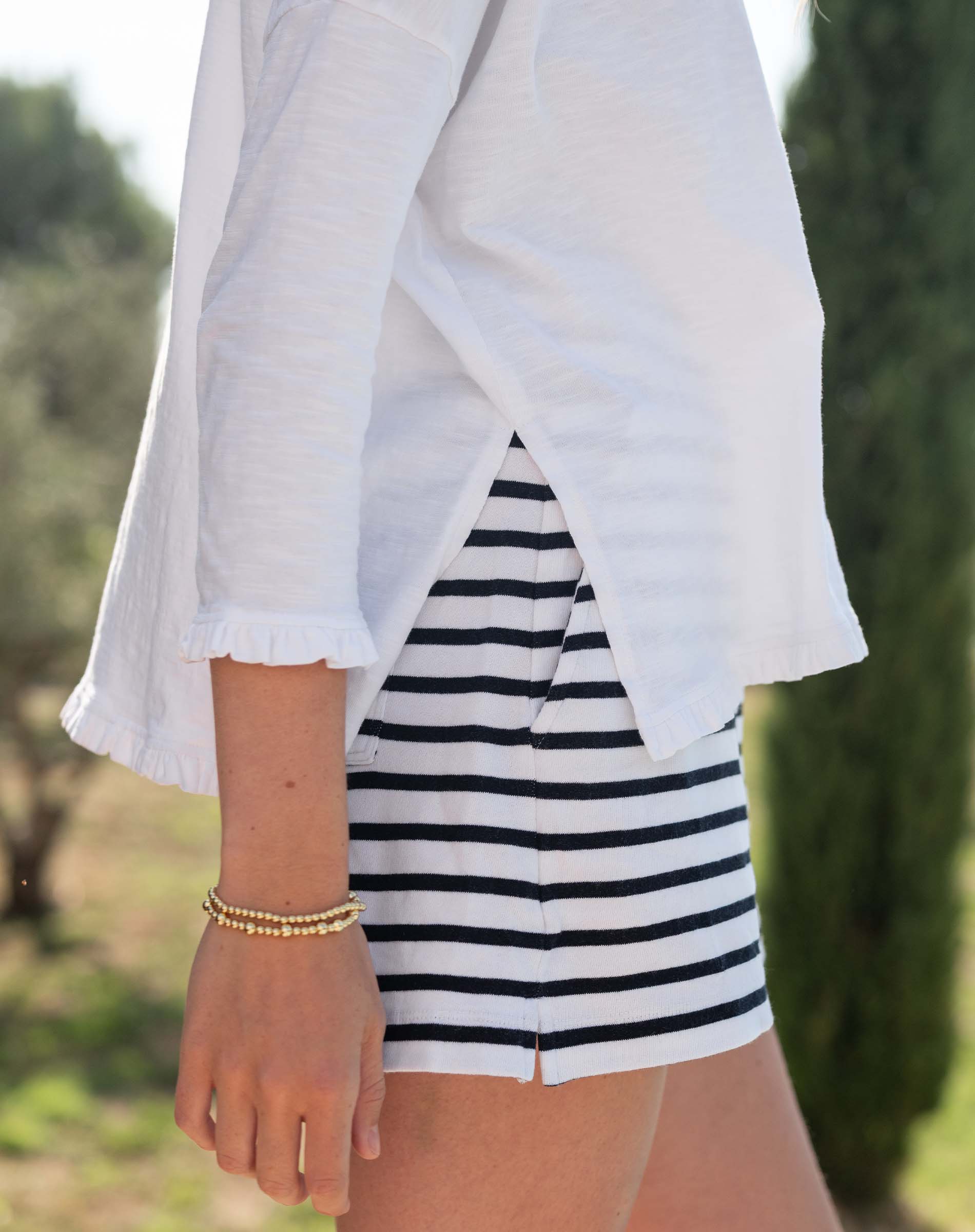 Person wearing a white shirt and black and white striped shorts with a blurred natural background