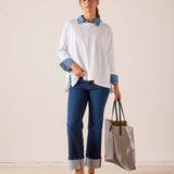 White ruffled tee with contrasting blue striped collar and cuffs, styled with blue denim jeans and a grey travel tote.