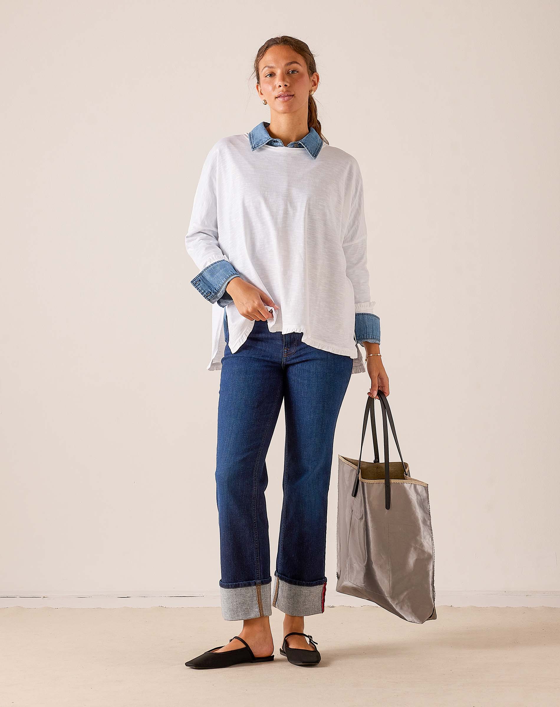 White ruffled tee with contrasting blue striped collar and cuffs, styled with blue denim jeans and a grey travel tote.