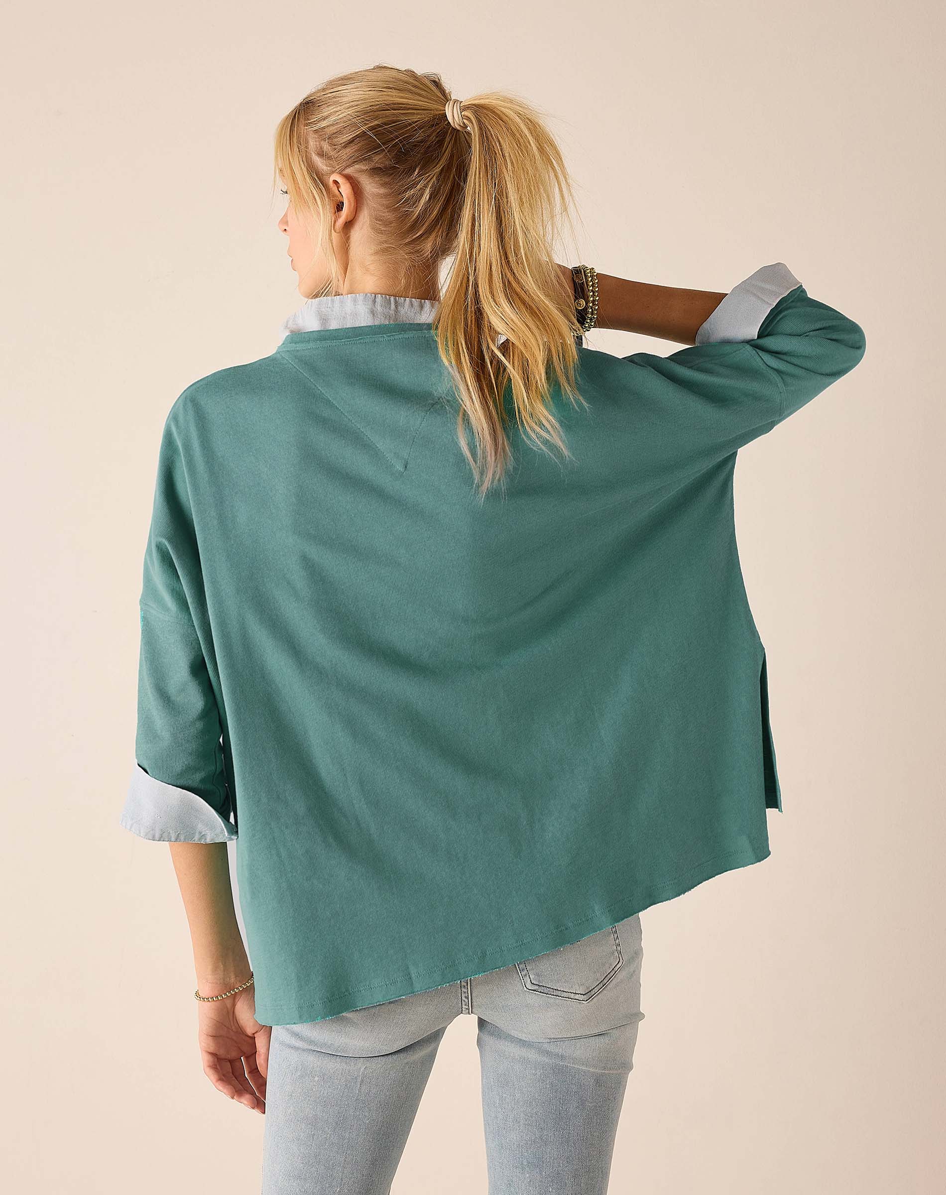 Back view of a woman wearing a women's travel-friendly aqua blue t-shirt with white contrast trim on the sleeves and hem.