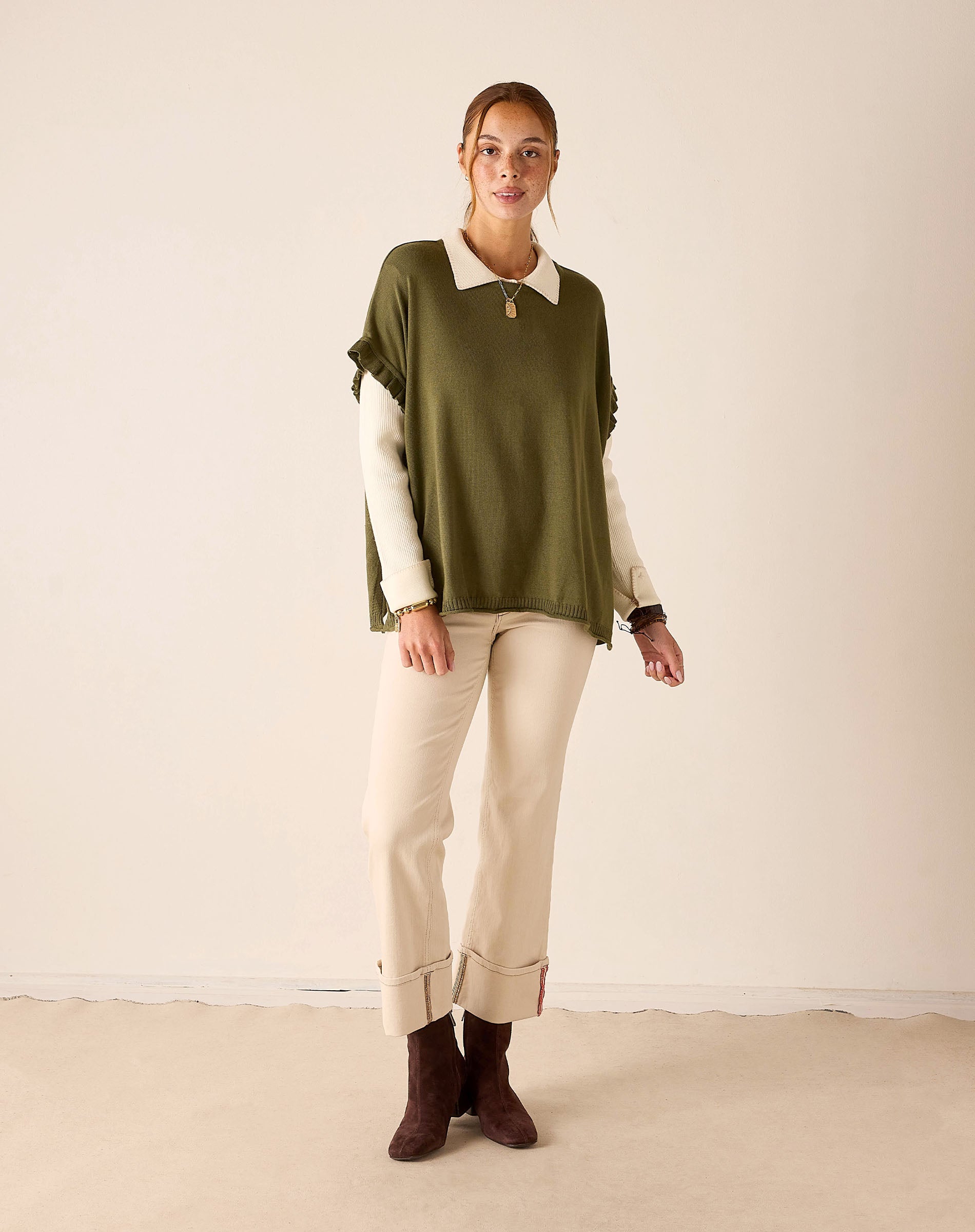 MERSEA women's travel-friendly moss green short-sleeve ruffle sweater layered over a white collared shirt and beige trousers.