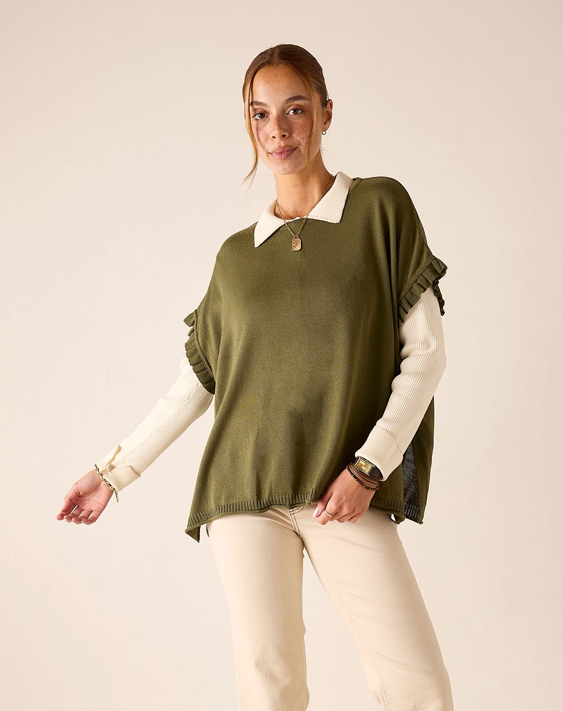 Moss green ruffled knit sweater worn over a white collared shirt with cream pants.