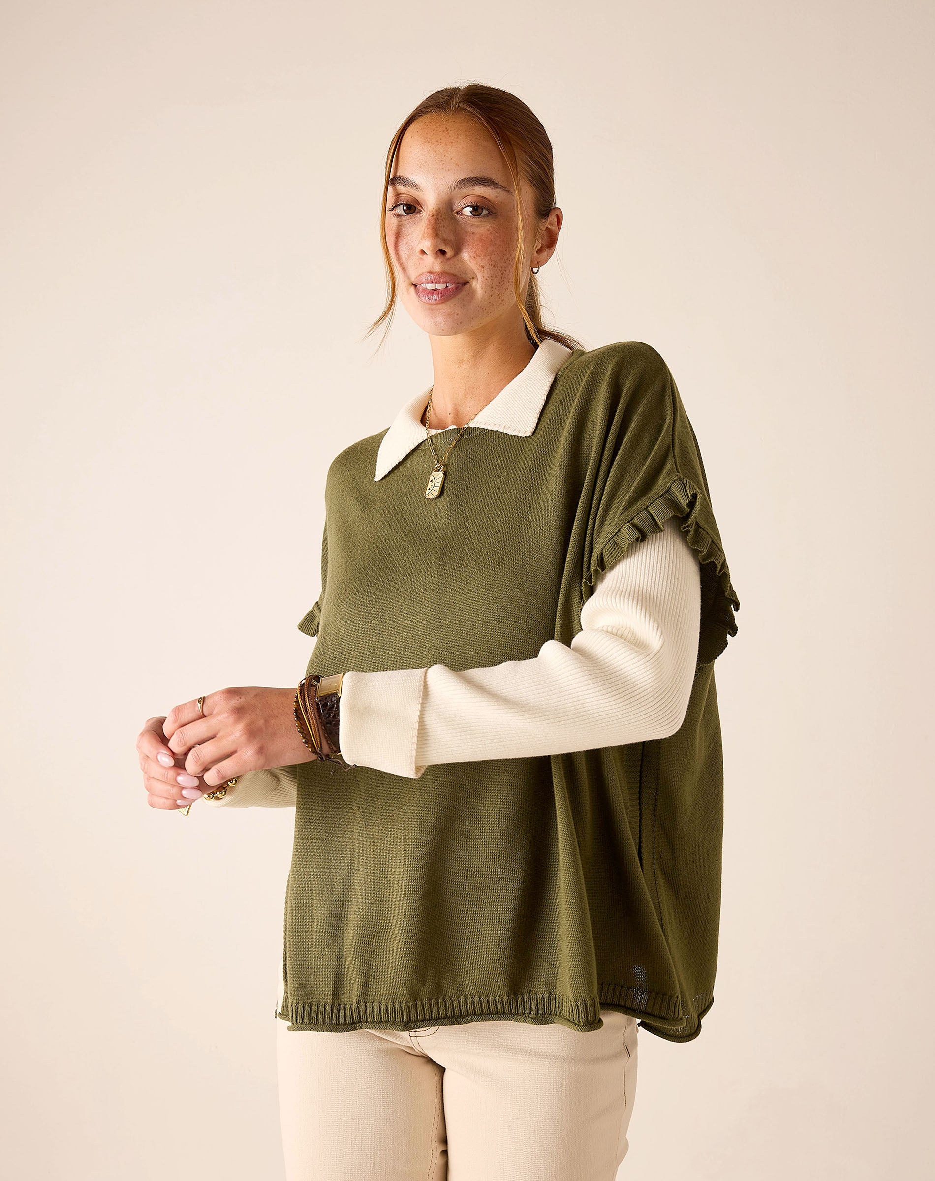 Moss green ruffled sweater worn over a cream-colored long-sleeved top.