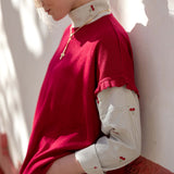 Jester red short-sleeved knit sweater over a white button-down shirt with small red embroidery.