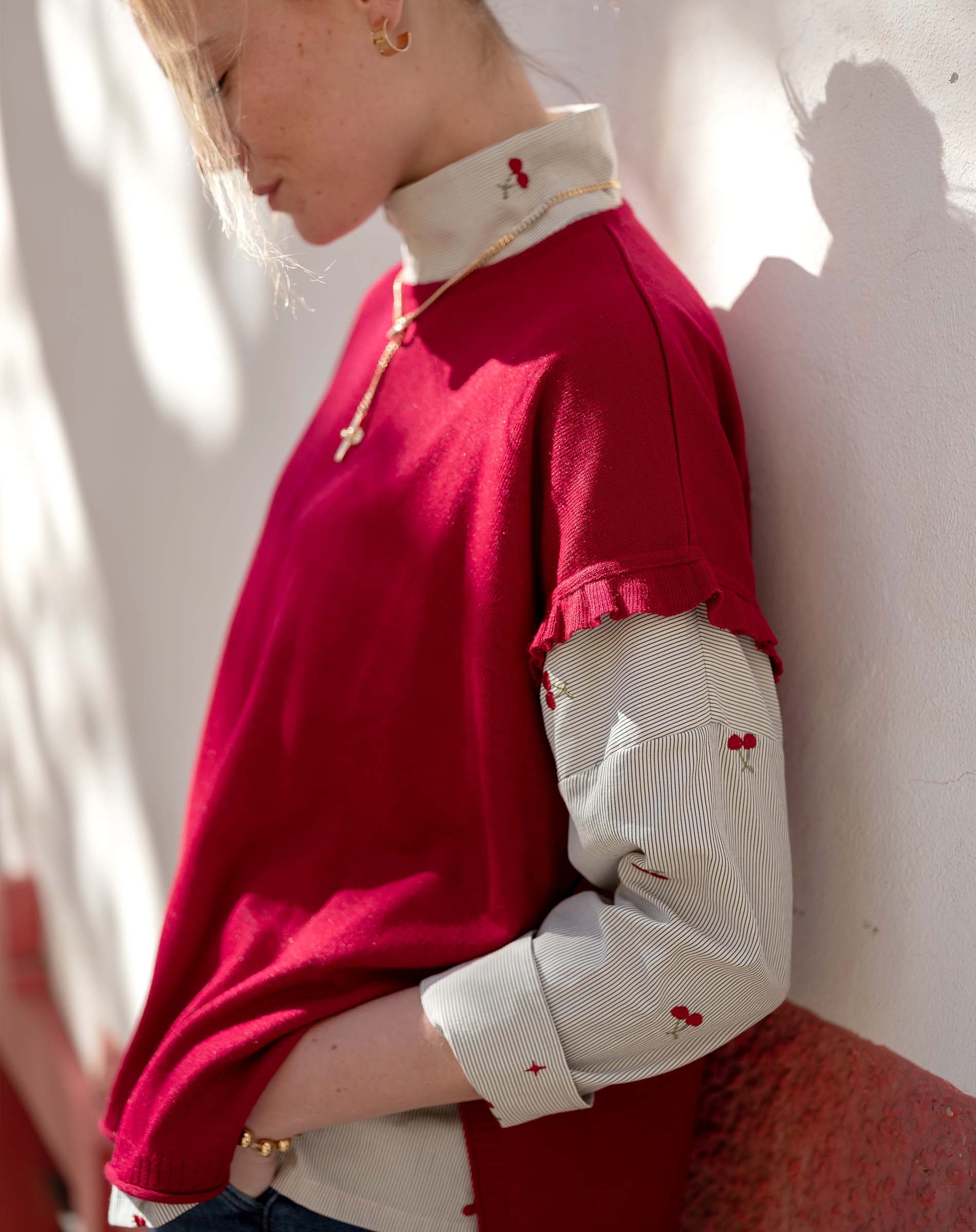 Jester red short-sleeved knit sweater over a white button-down shirt with small red embroidery.