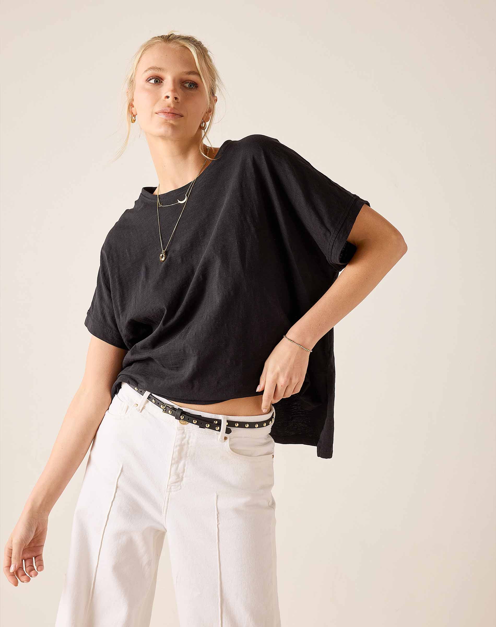 Woman wearing a black oversized t-shirt and white pants on a plain background