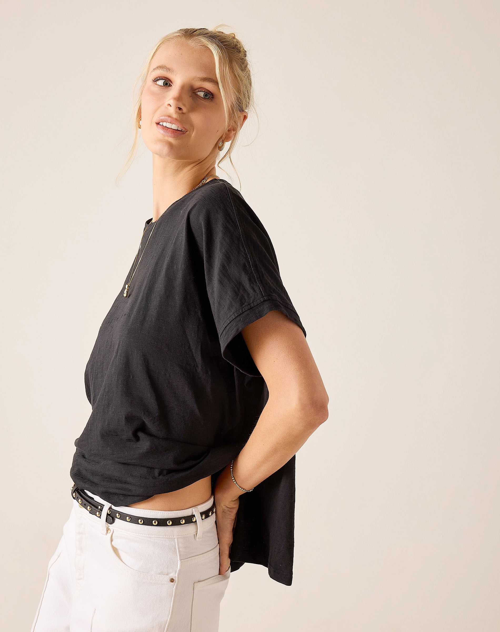 Woman wearing a black t-shirt and white pants against a plain background