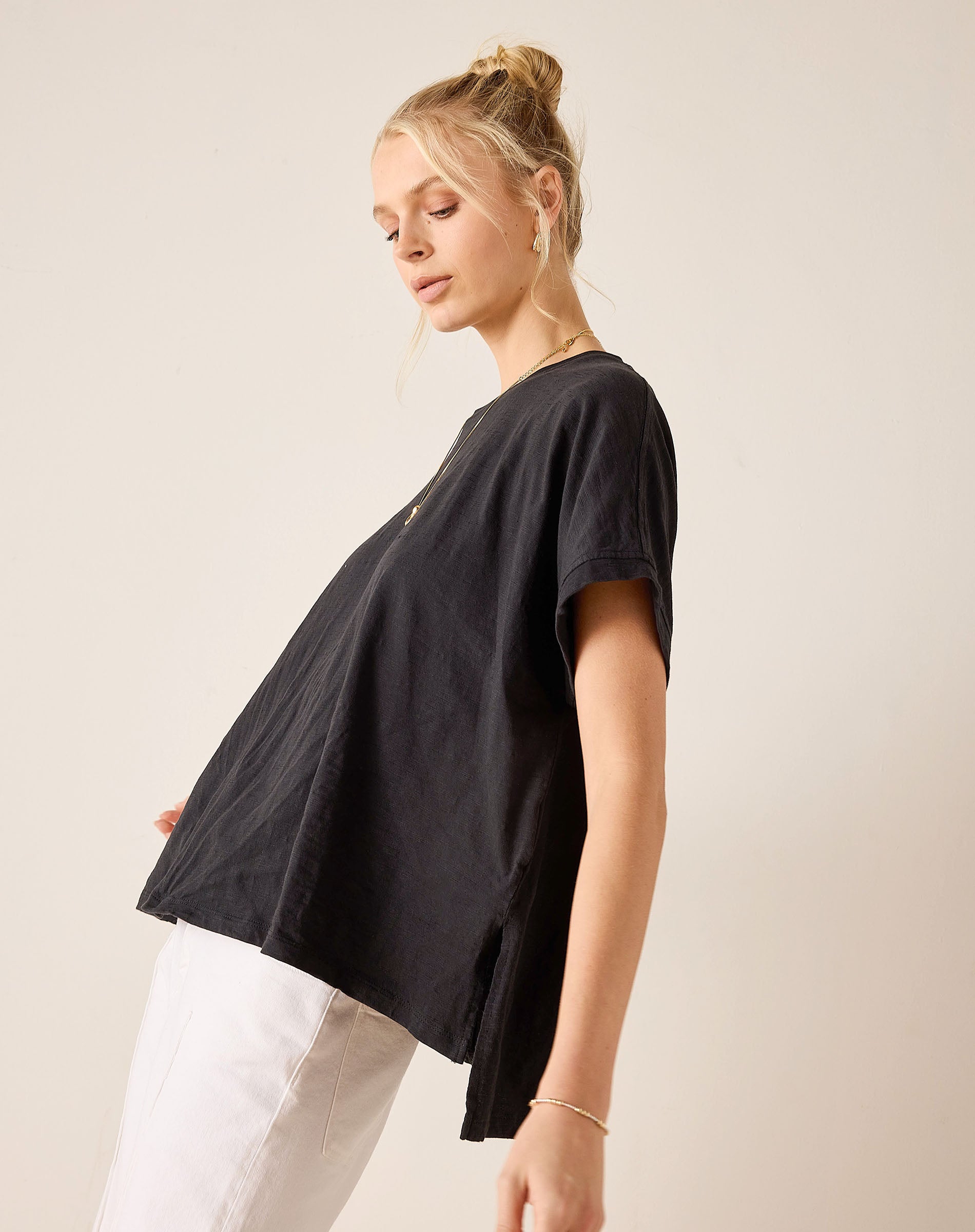 Woman wearing a black t-shirt and white pants against a plain background