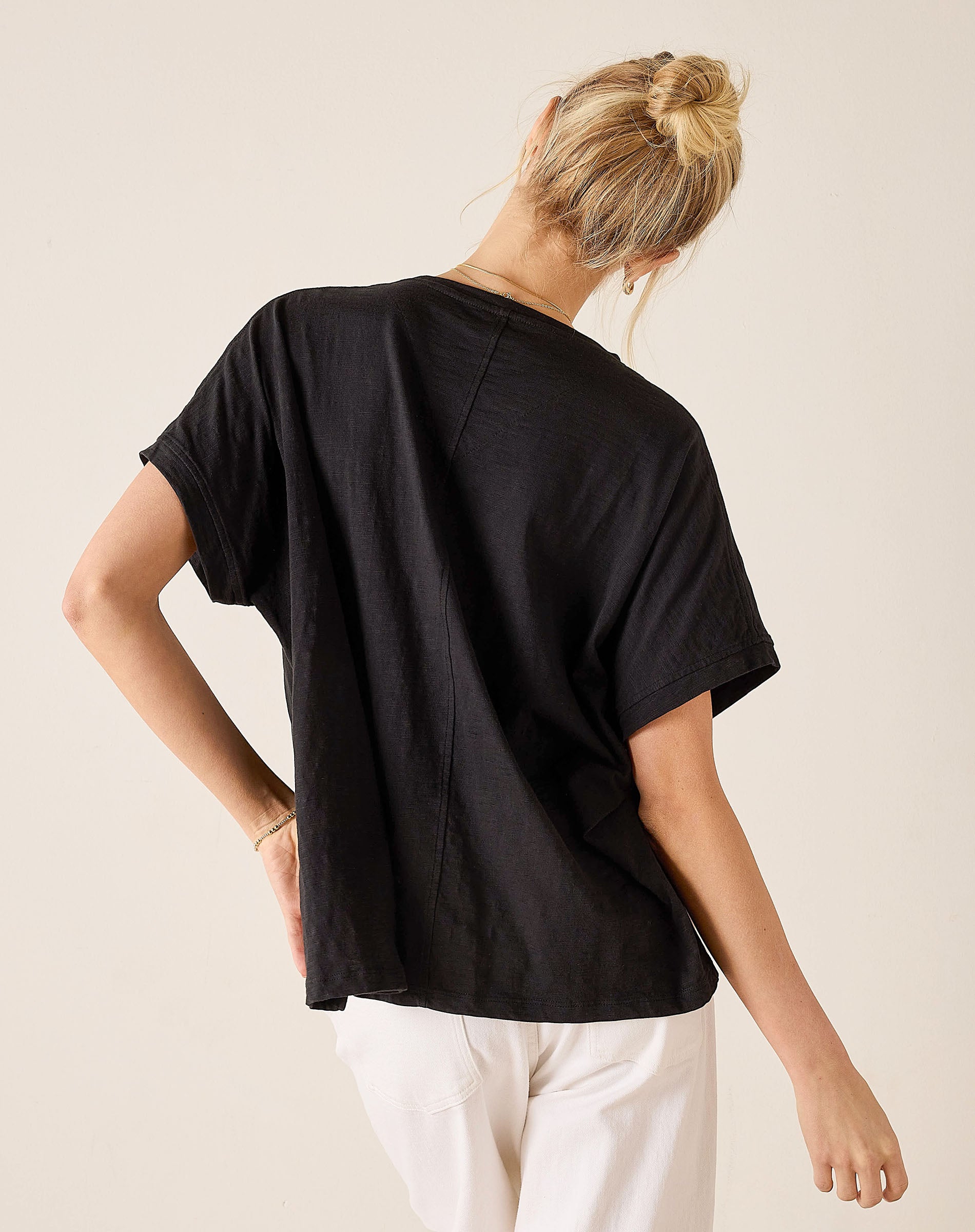 Person wearing a black t-shirt and white pants on a beige background