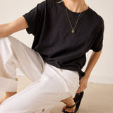 Person wearing a black t-shirt and white pants sitting on a beige floor.