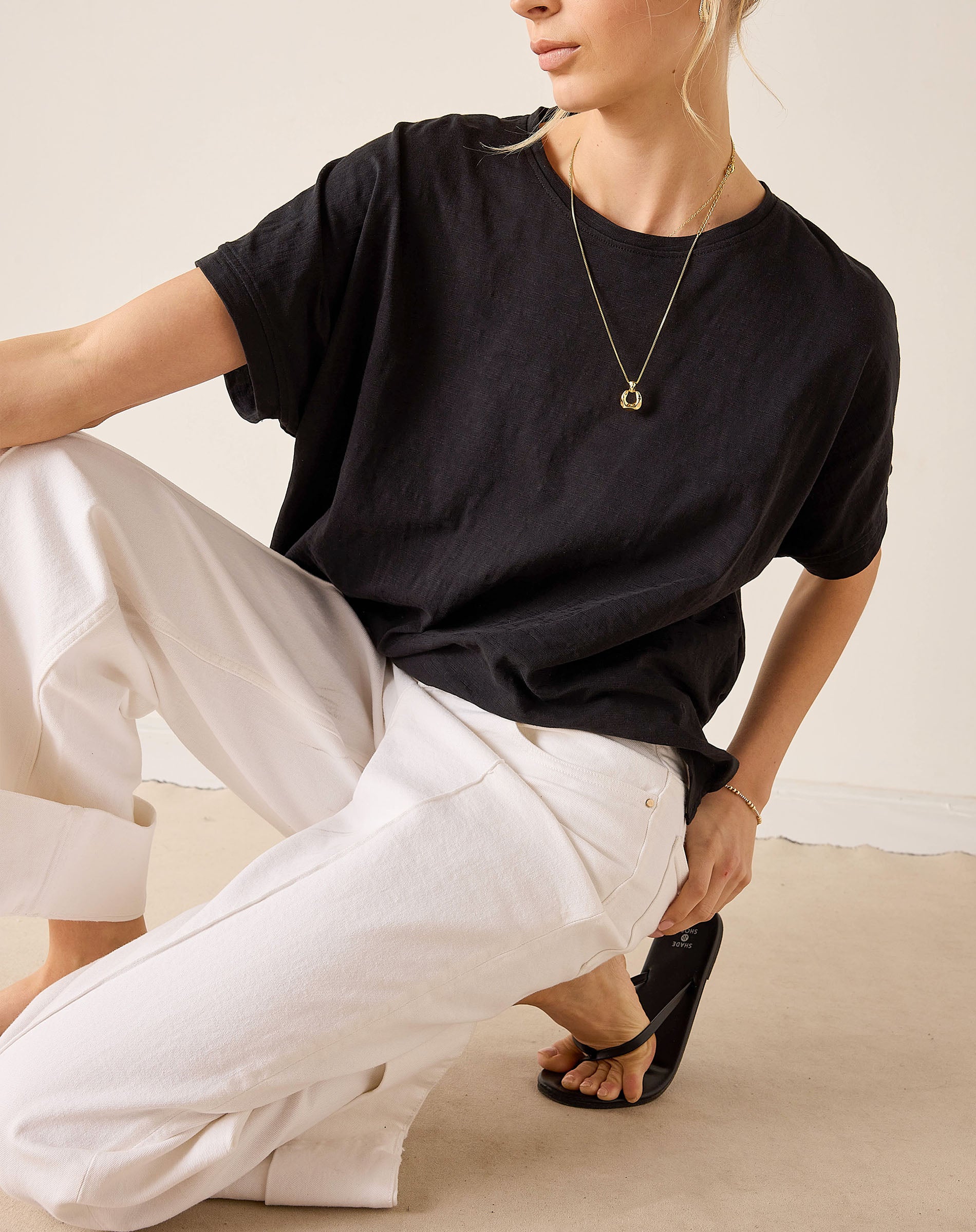 Person wearing a black t-shirt and white pants sitting on a beige floor.