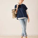 Woman wearing a navy blue top and light blue jeans, holding a beige tote bag against a plain background.