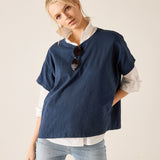 Woman wearing a navy blue sweater over a white shirt with light blue jeans on a beige background