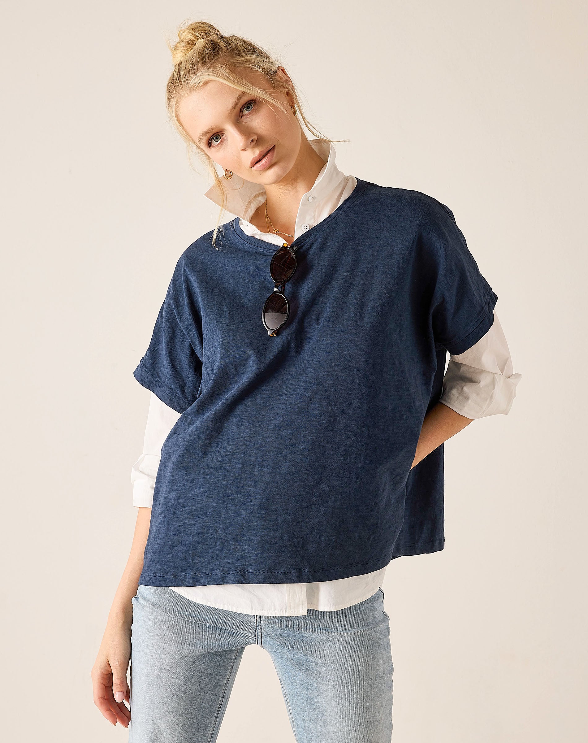 Woman wearing a navy blue sweater over a white shirt with light blue jeans on a beige background