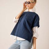 Woman wearing a navy blue poncho over a white shirt and light blue jeans, holding sunglasses.