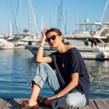 Navy blue oversized short-sleeve tee worn by a model on a dock near a boat harbor.